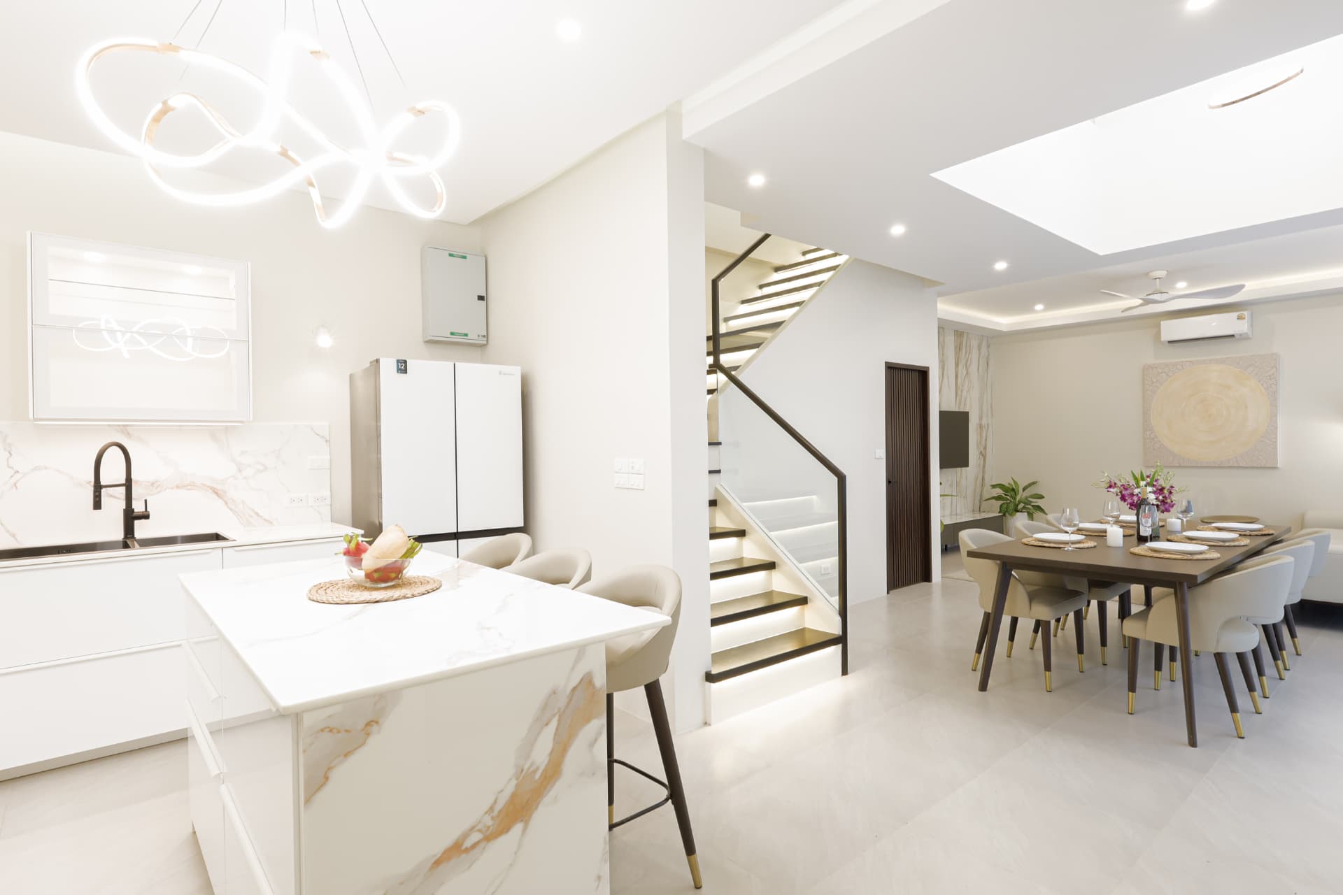 Open-plan kitchen with a marble island and bar stools, leading through to the staircase and dining area
