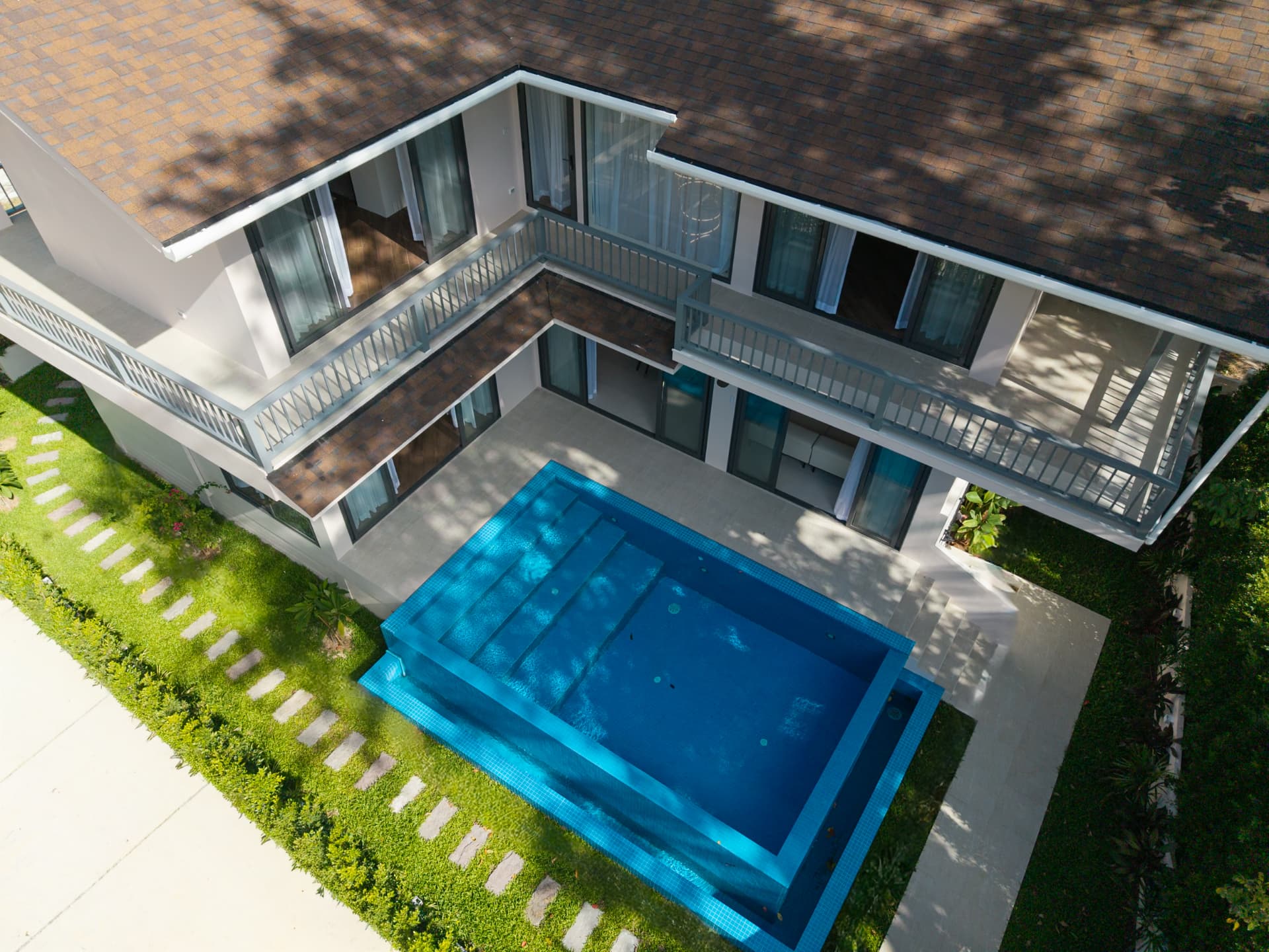 Aerial view of the villa's two storeys, balconies and the rectangular swimming pool surrounded by garden